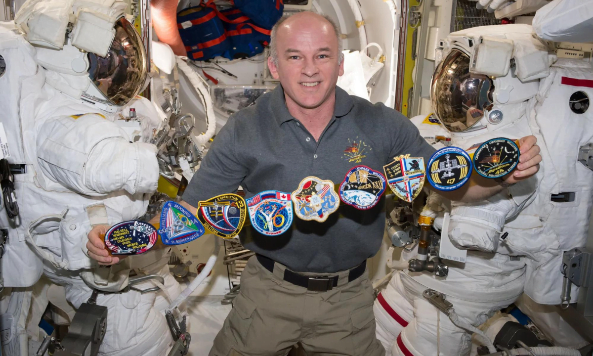 Commander Jeff Williams poses for a photo in the Quest Airlock (A/L) with all of his mission patches. The patches are, from left, STS-101, Soyuz TMA-8, Expedition 13, Soyuz TMA-16, Expedition 21, Expedition 22, Soyuz TMA-20M, Expedition 47, and Expedition 48.